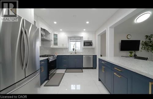 Modern kitchen featuring two-tone cabinetry, stainless steel appliances, a large center island with a stone-finish countertop, and recessed lighting - 643 Doon South Drive, Kitchener, ON 