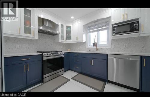 Kitchen featuring two-tone cabinetry, stainless steel appliances, patterned backsplash, light-toned countertops, and a built-in microwave - 643 Doon South Drive, Kitchener, ON 