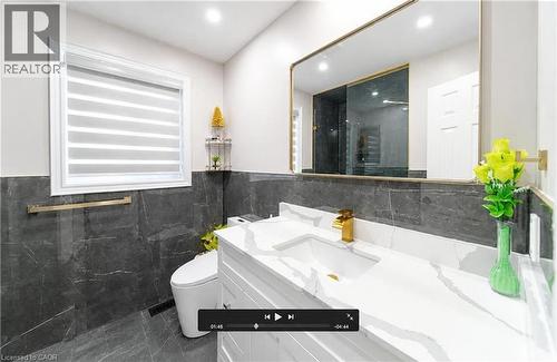 White vanity with integrated sink and gold-finish faucet, large framed mirror, and dark grey tile flooring - 643 Doon South Drive, Kitchener, ON 
