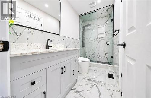 White shaker-style vanity with dark hardware, stone countertop, matte black faucet, full-height tiled shower with glass enclosure, and tiled flooring - 643 Doon South Drive, Kitchener, ON 