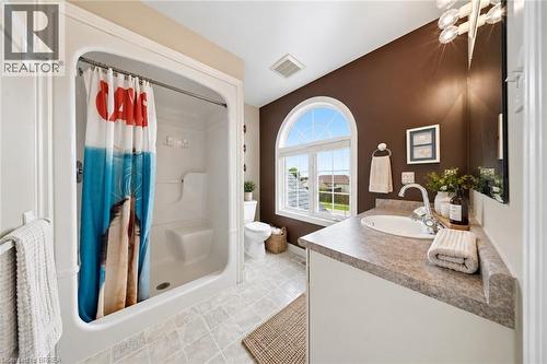 White integrated shower and tub combination, arched window with grid pattern, neutral-toned vanity with an integrated sink, polished chrome faucet, and tiled flooring - 61 Sunnyside Drive, St. George, ON 