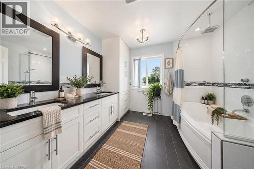 Dual vanity with integrated sinks, dark countertop, white cabinetry, separate walk-in shower with glass enclosure, and a built-in tub - 61 Sunnyside Drive, St. George, ON 