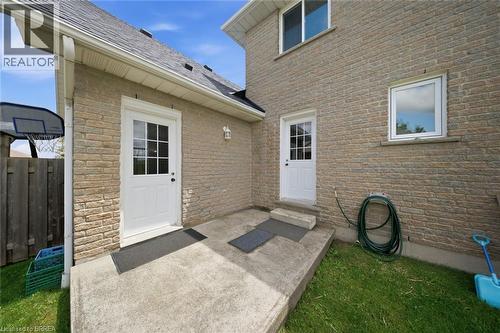 Brick exterior with two white exterior doors, concrete patio, and a shingled roof - 61 Sunnyside Drive, St. George, ON 