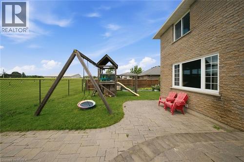 Stone block exterior with multiple windows, paver patio, and spacious lawn with chain link fencing - 61 Sunnyside Drive, St. George, ON 