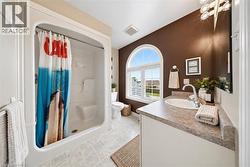 White integrated shower and tub combination, arched window with grid pattern, neutral-toned vanity with an integrated sink, polished chrome faucet, and tiled flooring - 