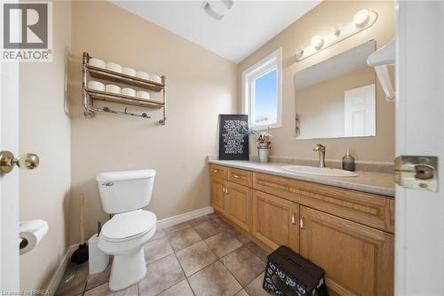 Bathroom featuring a light wood-finish vanity with an integrated sink, a large mirror, a window for natural light, and tile flooring - 61 Sunnyside Drive, St. George, ON 