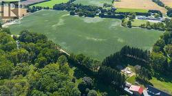 Expansive agricultural fields bordered by mature trees and additional wooded areas, featuring a large red-roofed structure - 