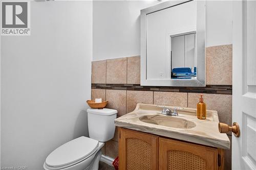 Bathroom featuring a single vanity with an integrated sink, polished chrome faucet, wood-finish cabinet, wall-mounted mirror, and tile wainscoting - 689 Barton Street E, Hamilton, ON 