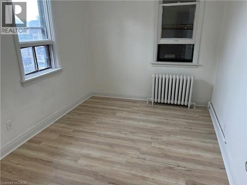 Wood-finish flooring with white baseboards, a white painted radiator, and two double-hung windows - 689 Barton Street E, Hamilton, ON 