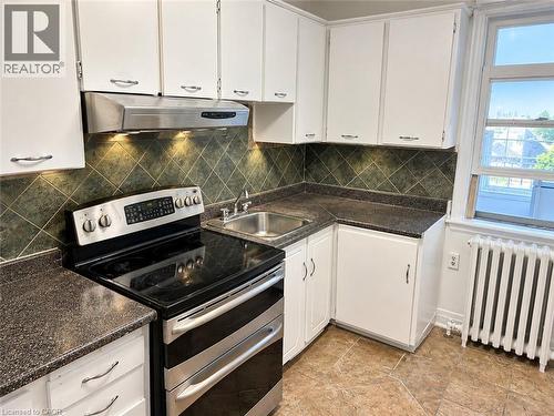 Kitchen featuring white cabinetry, a stainless steel range, a stainless steel range hood, dark countertops, and a tile backsplash - 689 Barton Street E, Hamilton, ON 