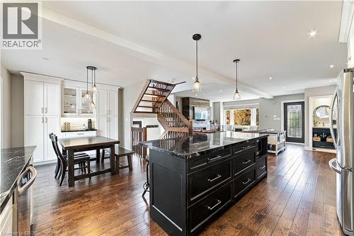 Open-concept kitchen with wood-finish flooring, a dark kitchen island with a granite countertop, and white cabinetry with granite countertop. Built in white cabinetry in dining area. - 58 Uplands Avenue, Hamilton, ON 