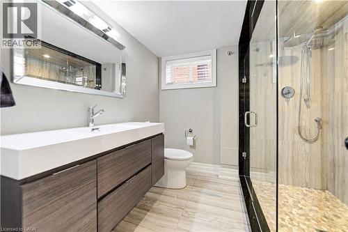 Floating wood-finish vanity, glass-enclosed shower with a rainfall showerhead, and a pebble tile shower floor.  Neutral ceramic flooring. - 58 Uplands Avenue, Hamilton, ON 
