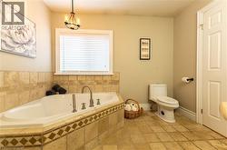Jetted soaking tub with a tiled surround, complete with a window and a ceiling-mounted light fixture - 