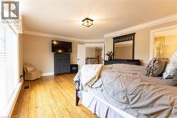 Spacious room featuring wood-finish flooring, abundant natural light from large windows, crown molding, and a ceiling-mounted fixture - 