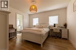 Bright, neutral bedroom showcasing hardwood flooring, two large windows with plantation shutters, a woven rattan pendant light fixture, and ample natural light - 