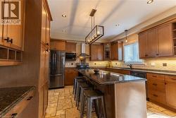 Kitchen featuring extensive wood cabinetry, stone tile flooring, stainless steel appliances, a large center island with counter seating, and recessed lighting - 