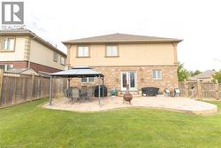 Expansive backyard featuring a manicured lawn, a large paver patio, full-height privacy fencing, and a two-story exterior with brick and stucco finishes - 