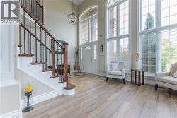 Two-story entryway with wood-finish flooring, a grand staircase featuring wood treads and wrought iron spindles, a two-story arched window, and a modern chandelier - 