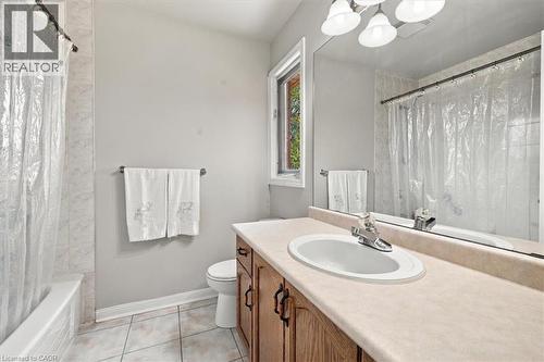 Bathroom featuring a built-in vanity with wood-finish cabinetry, a single basin sink, a large wall-mounted mirror, and tile flooring - 5180 Oakley Drive, Burlington, ON 