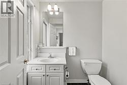 White paneled door opening to a bathroom featuring a white vanity with an integrated sink, a vanity mirror with sconce lighting, and a white toilet - 