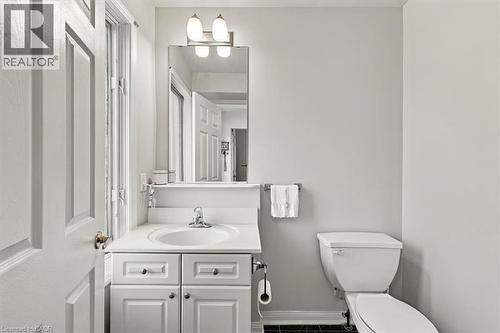 White paneled door opening to a bathroom featuring a white vanity with an integrated sink, a vanity mirror with sconce lighting, and a white toilet - 5180 Oakley Drive, Burlington, ON 