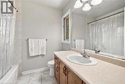 Bathroom featuring a built-in vanity with wood-finish cabinetry, a single basin sink, a large wall-mounted mirror, and tile flooring - 