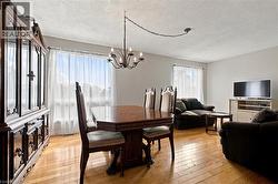 Wood-finish flooring throughout, featuring a chandelier above the dining area and large windows - 