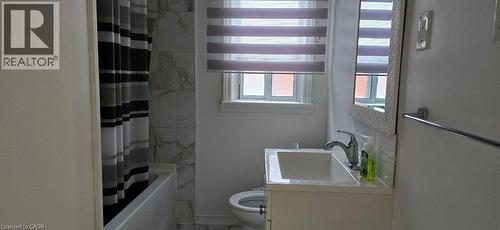 White vanity with integrated sink, chrome faucet, window with privacy blinds, white subway tile backsplash, and full wall tile surround in the shower - 284 Brucedale Avenue E, Hamilton, ON 