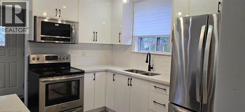 Kitchen featuring white cabinetry with black hardware, stainless steel appliances, a white subway tile backsplash, and light-toned countertops - 284 Brucedale Avenue E, Hamilton, ON 