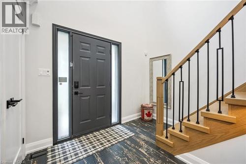 Entryway featuring a dark paneled door with frosted sidelights, a natural wood staircase with black iron balusters, and distressed wood-finish flooring - 1261 Stephenson Drive, Burlington, ON 