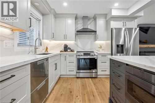 Light-toned wood-finish flooring, white cabinetry with matte black hardware, stainless steel appliances, white countertops, and a white backsplash with veining - 1261 Stephenson Drive, Burlington, ON 