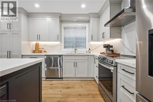 Contemporary kitchen featuring light gray cabinetry, stainless steel appliances, wood-finish flooring, and light-toned countertops with a matching backsplash - 1261 Stephenson Drive, Burlington, ON 