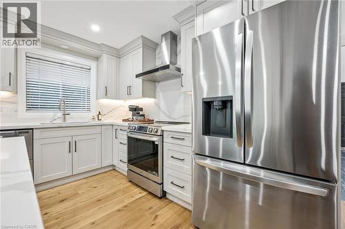 Modern kitchen featuring light-toned cabinetry with dark hardware, stainless steel appliances, quartz countertops with a matching backsplash, and wood-finish flooring - 1261 Stephenson Drive, Burlington, ON 