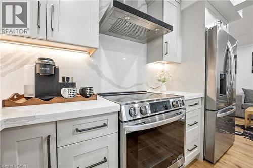 Light-toned cabinetry with dark hardware, quartz countertops, tile backsplash, built-in stainless steel oven with cooktop, and stainless steel refrigerator - 1261 Stephenson Drive, Burlington, ON 