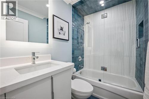 Contemporary vanity with integrated sink and chrome faucet, backlit mirror, and a shower-tub combination featuring textured white tile and blue mosaic tile accents - 1261 Stephenson Drive, Burlington, ON 