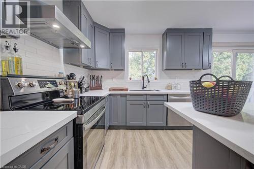 U-shaped kitchen featuring grey cabinetry, white countertops, wood-finish flooring, a tile backsplash, and stainless steel appliances - 317 Christopher Drive, Cambridge, ON 