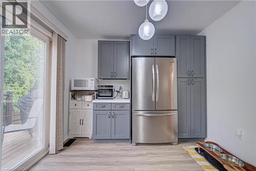 Gray shaker-style cabinetry, stainless steel refrigerator, white countertops, wood-finish flooring, and sliding glass door - 317 Christopher Drive, Cambridge, ON 