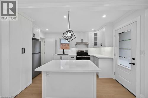 Kitchen featuring a central island, white cabinetry with black hardware, stainless steel appliances, light-toned flooring, and a glass-paneled exterior door - 50 West 4Th Street, Hamilton, ON 