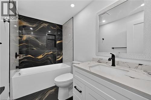 Built-in bathtub with a black and gold marbled tile surround, white vanity with a white countertop and integrated sink, matte black faucet, and a decorative framed mirror - 50 West 4Th Street, Hamilton, ON 