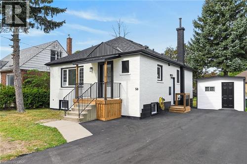 Charming cottage-style residence featuring a freshly paved asphalt driveway, modern black metal railings with wooden accents at the entrance, and a pyramidal roof with dark architectural shingles - 50 West 4Th Street, Hamilton, ON 
