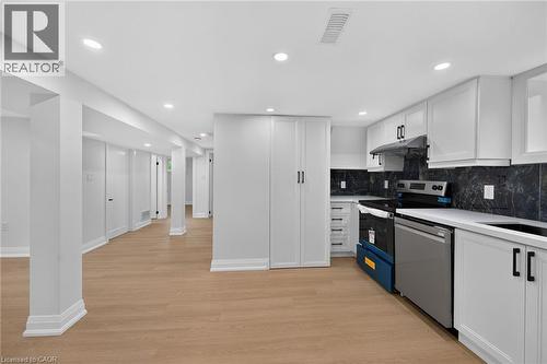Modern kitchen and open floor plan featuring white cabinetry with hardware accents, stainless steel appliances including a gas range and dishwasher, dark tile backsplash, white quartz countertops, rec - 50 West 4Th Street, Hamilton, ON 