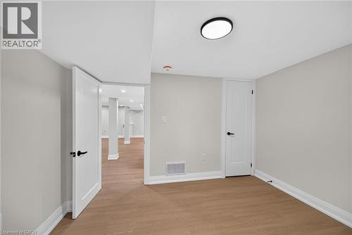 Light wood-finish flooring, white doors with matte black hardware, and a flush-mount ceiling light fixture - 50 West 4Th Street, Hamilton, ON 