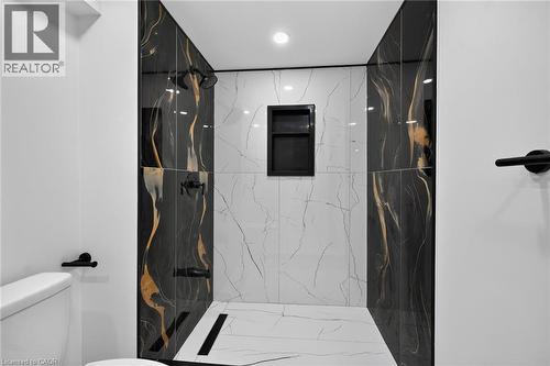 Tiled shower stall with black and white veined tile, contrasting black and gold accent tiles, matte black shower fixtures, and a recessed shower niche - 50 West 4Th Street, Hamilton, ON 