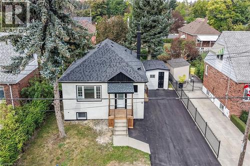 White exterior with a dark shingled roof, featuring a paved driveway and an accompanying shed - 50 West 4Th Street, Hamilton, ON 