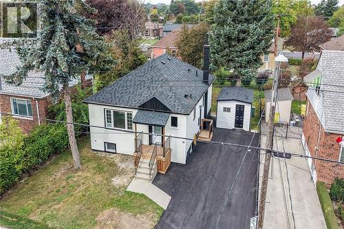 White exterior with black trim, dark shingle roof, front entrance with wood-finish decking and railing, concrete steps, and a paved driveway - 50 West 4Th Street, Hamilton, ON 