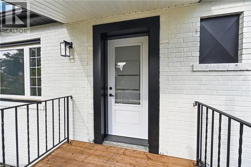 White painted brick exterior with black trim, a wood-finish porch, and black metal railings - 50 West 4Th Street, Hamilton, ON 