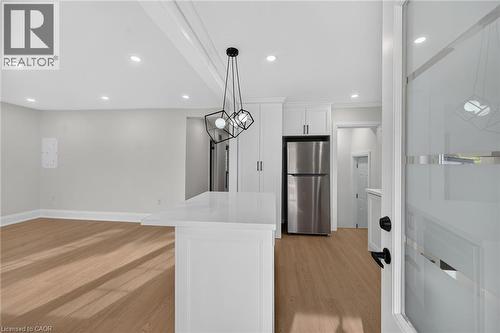 Wood-finish flooring, recessed ceiling lighting, kitchen island with a white countertop, modern geometric pendant lighting, and stainless steel refrigerator - 50 West 4Th Street, Hamilton, ON 