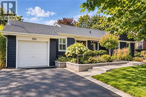 Shingle siding in a dark blue hue, white garage door, asphalt driveway, stone retaining wall, and mature landscaping - 896 Eagle Drive, Burlington, ON 