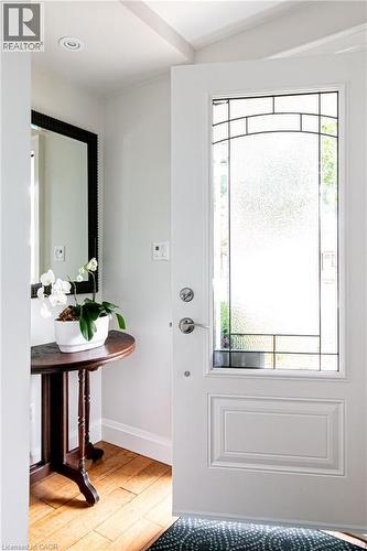 Entryway featuring wood-finish flooring, a decorative half-moon table, and a white paneled door with an integrated leaded glass insert - 896 Eagle Drive, Burlington, ON 