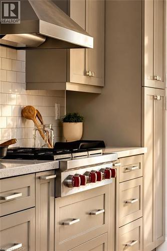 Stainless steel range with red control knobs, complementing a stainless steel range hood - 896 Eagle Drive, Burlington, ON 